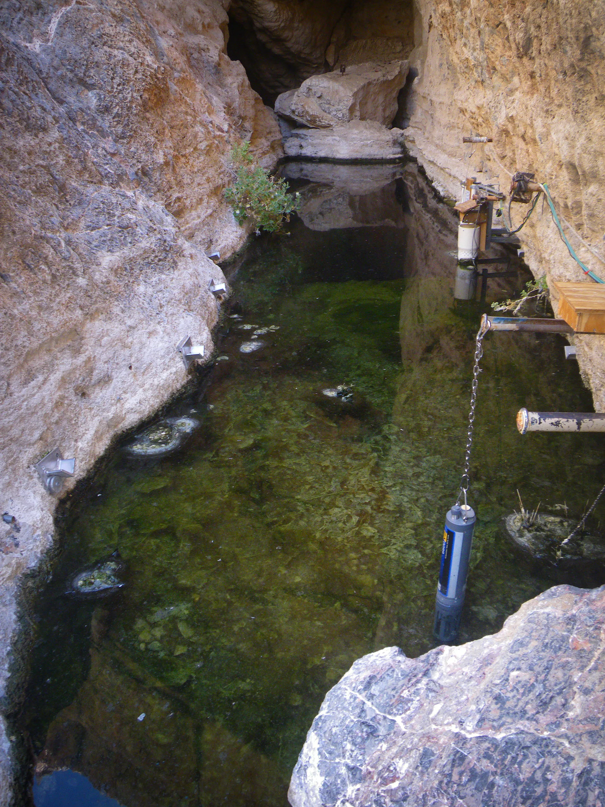 Vue plongeante sur une étroite fissure rocheuse au fond de laquelle s’étend une eau sombre et verte.