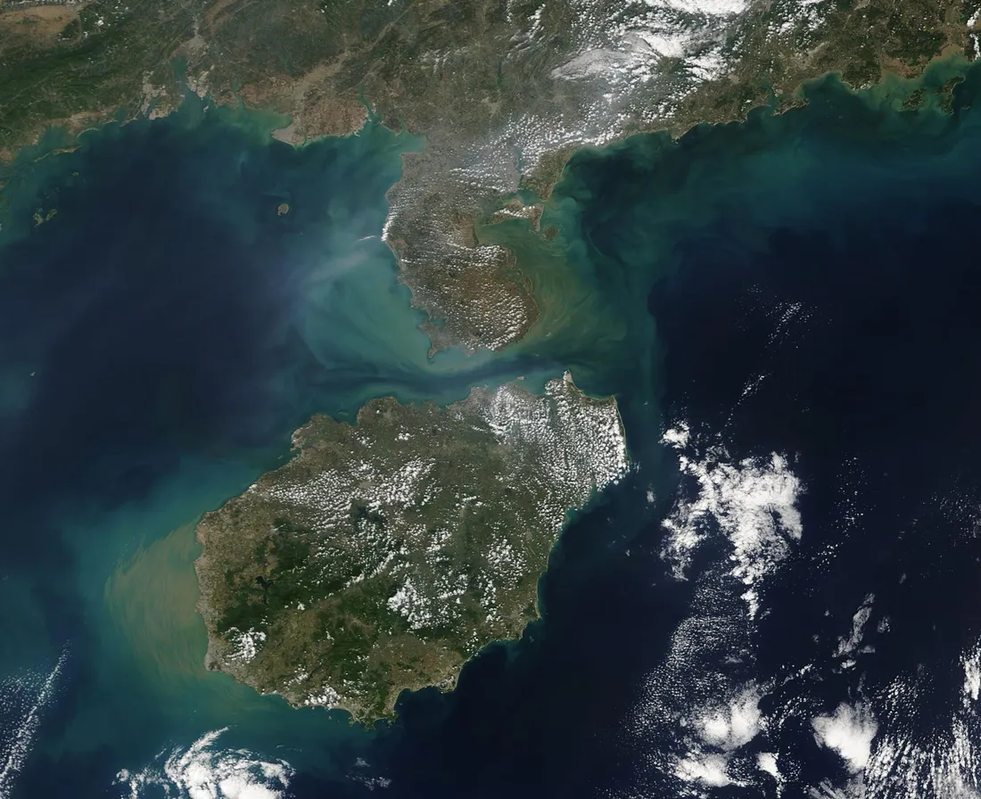 Vue satellite de l'île de Hainan, verte et en partie couverte de nuages, au sud de la côte chinoise.